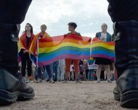 Police officers watch as people wave rainbow flags